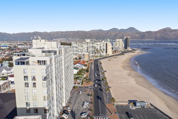 A coastal cityscape with high-rise buildings, a beach, and mountains in the background.