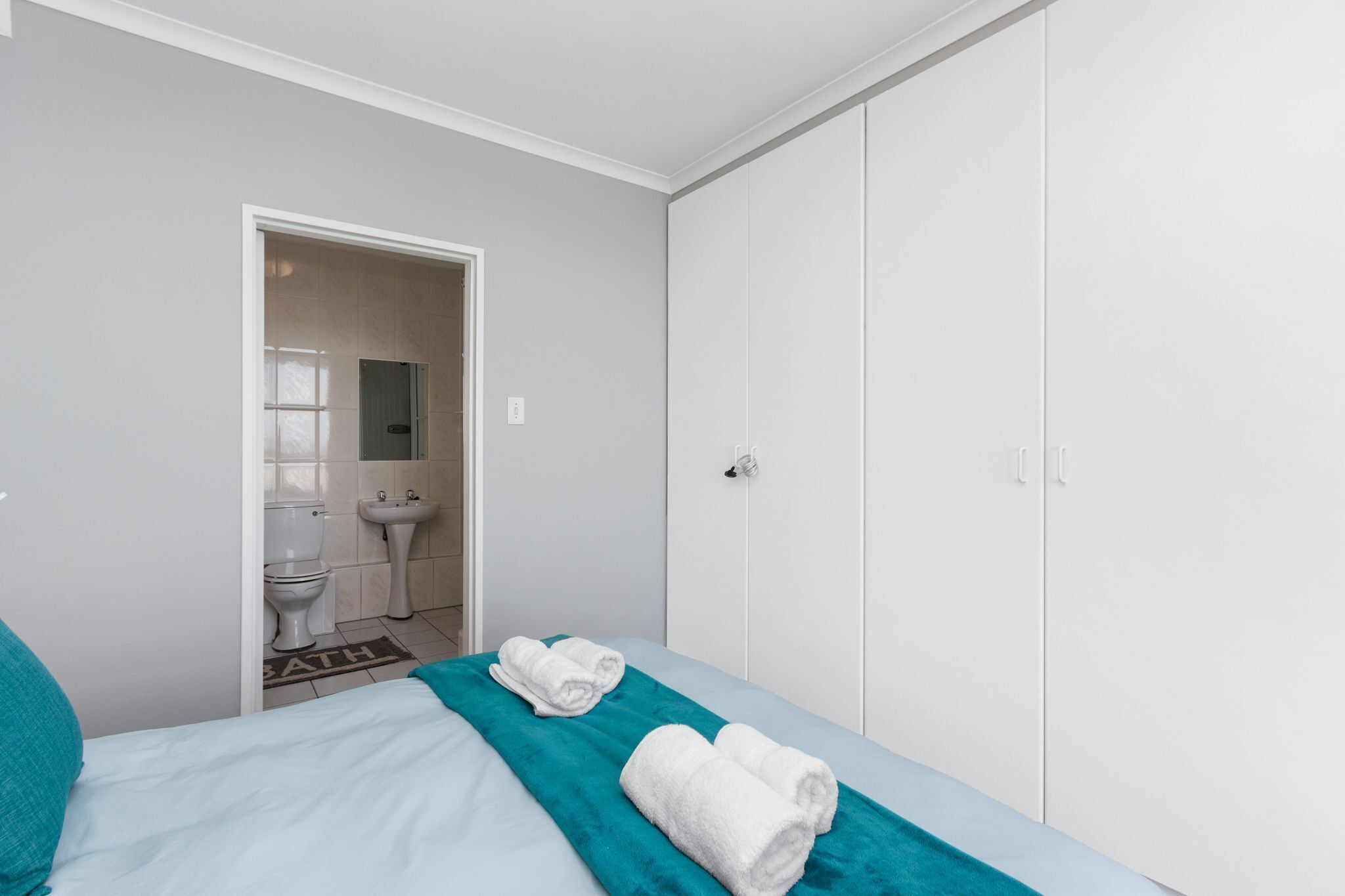 A bedroom with a bed, a bathroom visible through an open door, and a wardrobe.