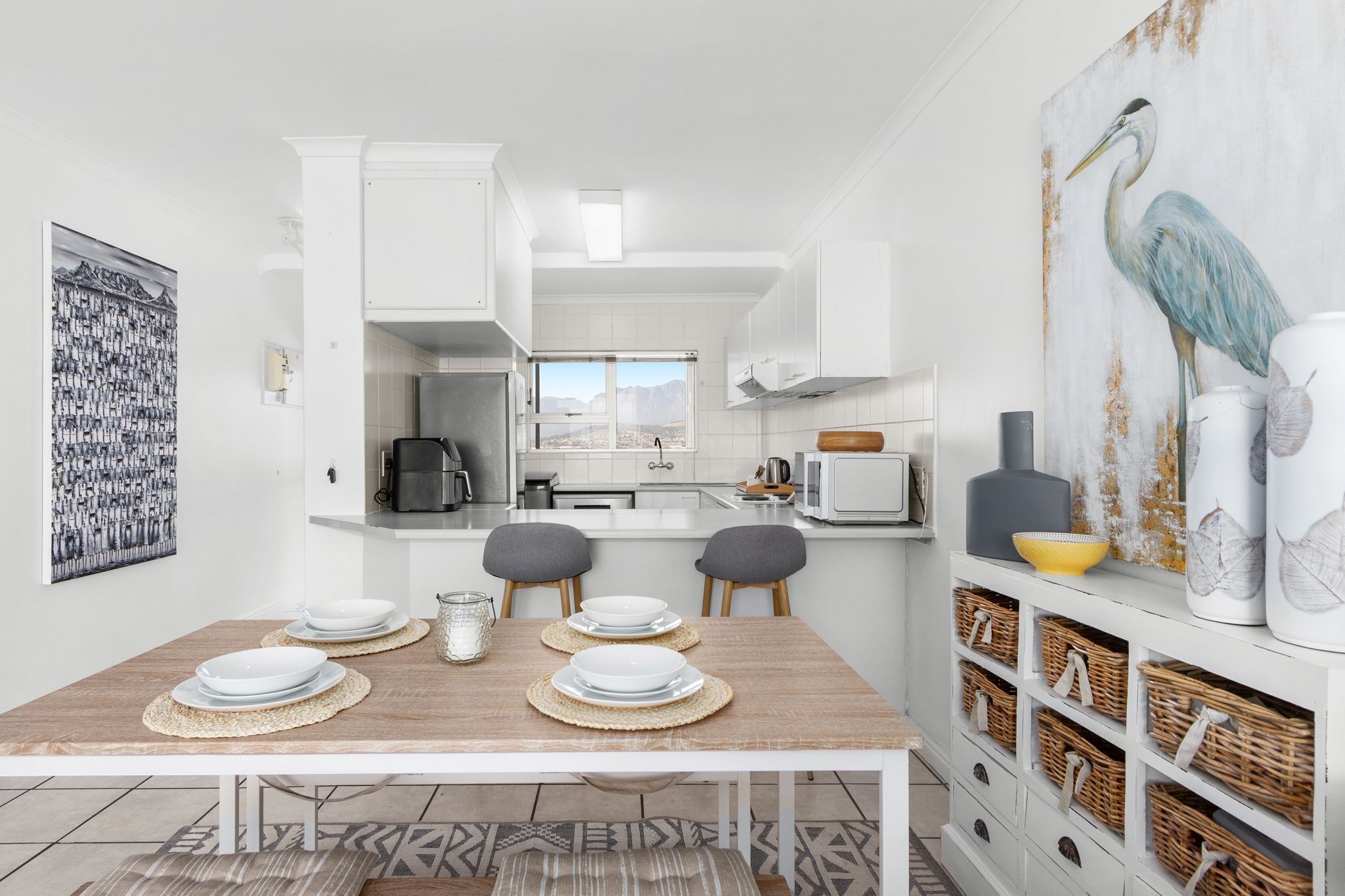 A modern kitchen with white cabinetry, a dining table set with plates and a coffee machine.