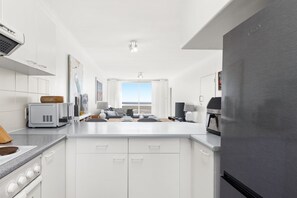 A modern kitchen with white cabinetry, a stainless steel refrigerator, and a view to the outside. - Odeon Towers 1102 (Cape Town)