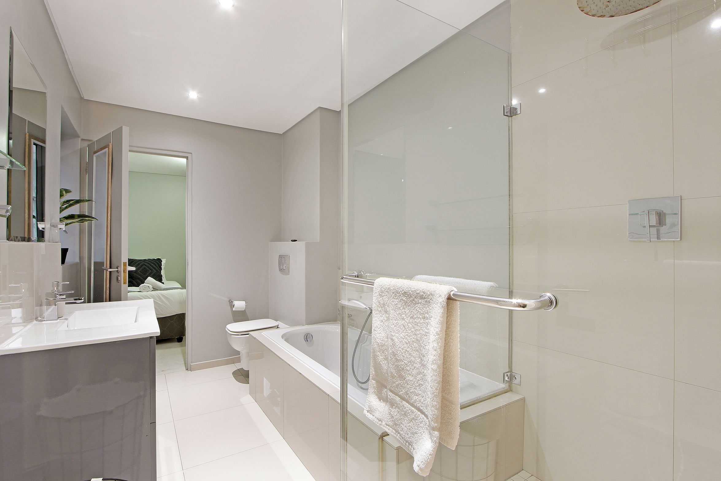A modern bathroom with a glass shower enclosure, a white bathtub, and a vanity with a mirror.