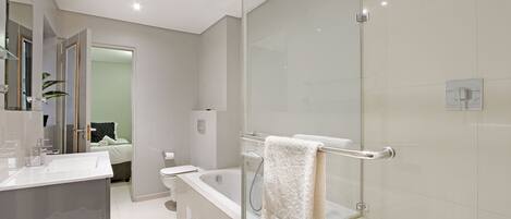A modern bathroom with a glass shower enclosure, a white bathtub, and a vanity with a mirror.