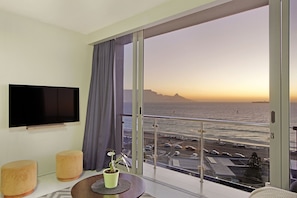 Habitación de hotel moderna con un balcón grande, televisión de pantalla plana y vistas al océano y al estacionamiento.
