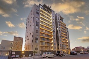 A multi-story residential building with balconies, a gated entrance, and several parked cars. - Infinity 404 (Cape Town)