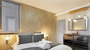 A bedroom with a large bed, a dresser, a mirror, and a bedside lamp.