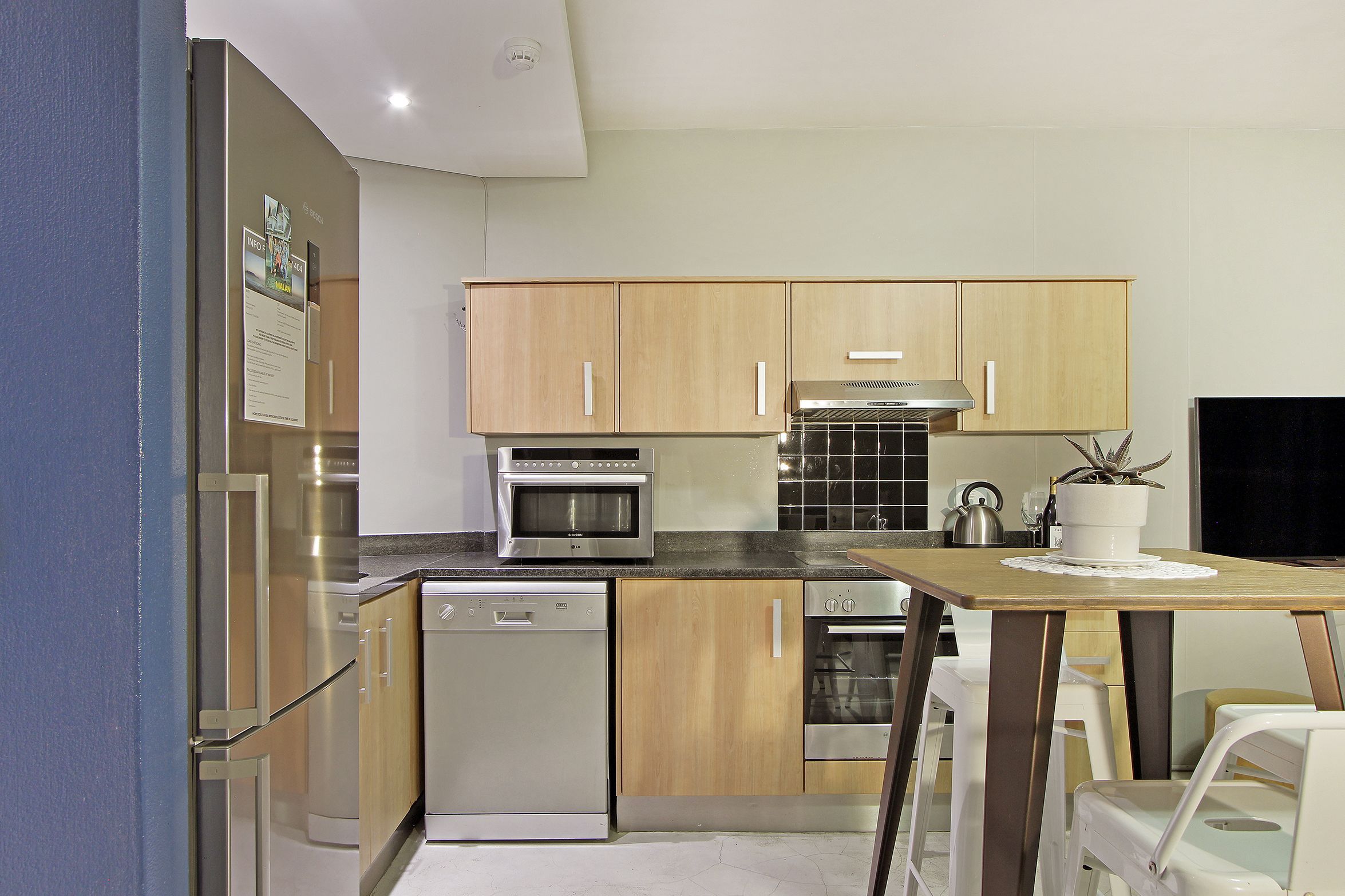 A compact kitchen with wooden cabinets, a built-in oven, a dishwasher, and a dining table with chairs.