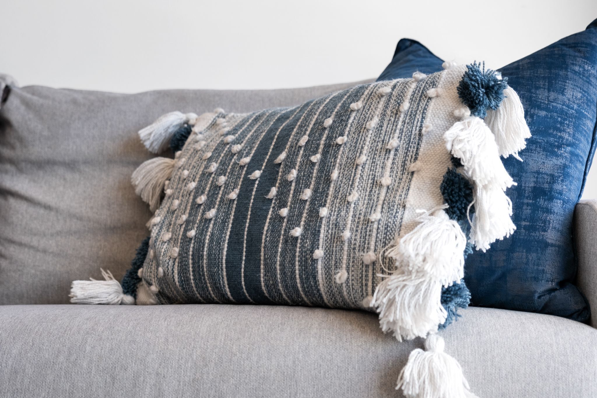 A grey sofa with a striped pillow and tassels.