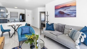 Una sala moderna con un sofá gris, sillones azules y una mesa de centro con un jarrón de flores.