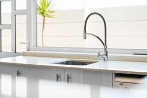 A kitchen with a stainless steel sink, white cabinets, and a window with a view of a palm tree.