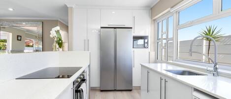 A modern kitchen with white cabinetry, a stainless steel refrigerator, a built-in oven, and a window with a view of the outside.
