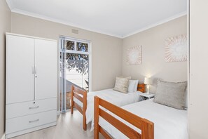 A bedroom with two single beds, a wardrobe, a desk, and a window with a view of trees. - Ravens 9A (Cape Town)