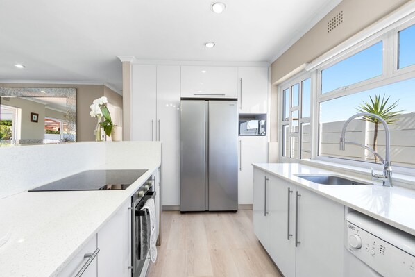 A modern kitchen with white cabinetry, a stainless steel refrigerator, a built-in oven, and a window with a view of the outside.