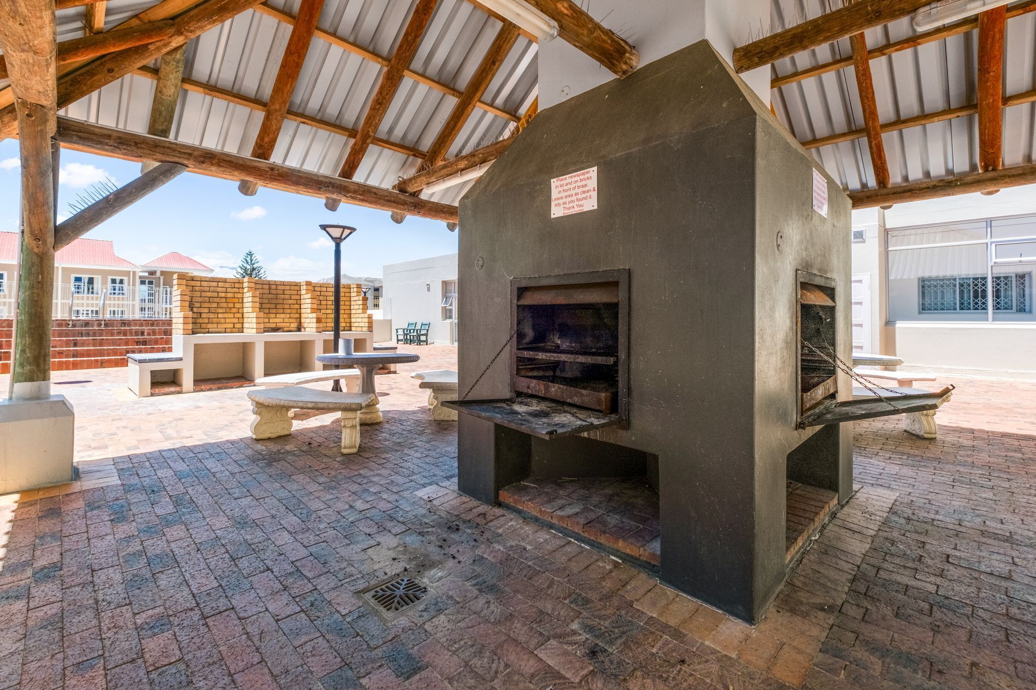 An outdoor patio with a brick floor, wooden benches, and a large stone fireplace.