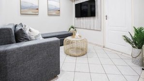 Un salon moderne avec un canapé gris, une table basse ronde en osier et une plante en pot.