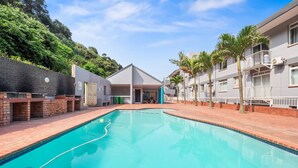 A swimming pool with a brick border, surrounded by a brick wall and a building with a flat roof. - Cozumel 308 (eMdloti)