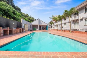 A swimming pool with a brick border, surrounded by a brick wall and a building with a flat roof. - Cozumel 308 (eMdloti)