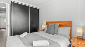 A neatly made bed with a grey blanket and a rolled white towel, a wooden headboard, two bedside lamps, and a sliding door closet. - Cozumel 308 (eMdloti)