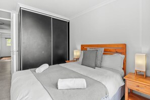 A neatly made bed with a grey blanket and a rolled white towel, a wooden headboard, two bedside lamps, and a sliding door closet. - Cozumel 308 (eMdloti)