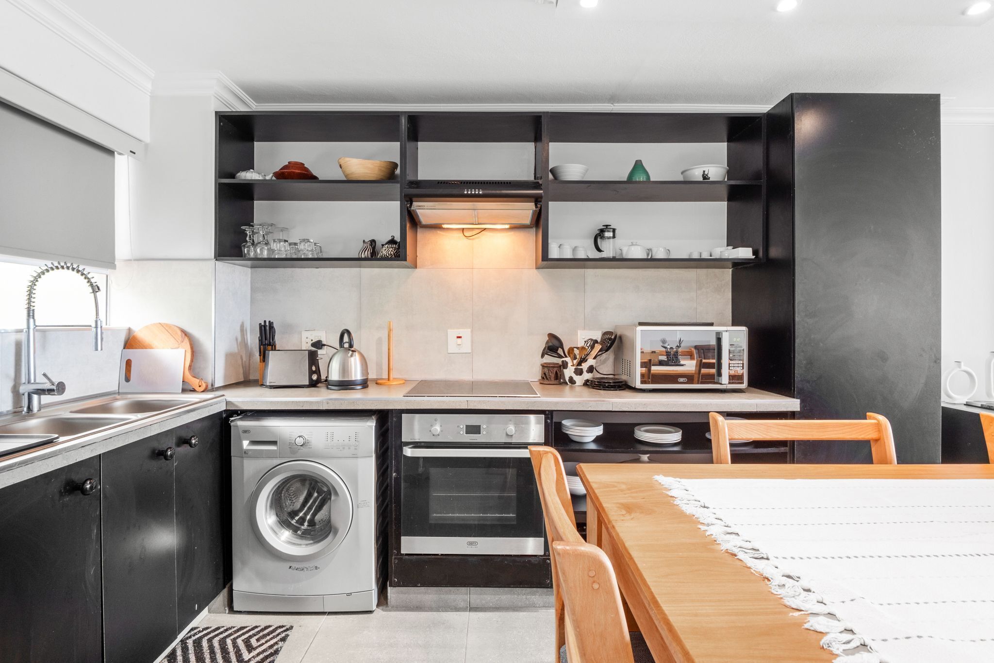 A modern kitchen with built-in appliances, a dining area with a table and chairs, and a washing machine.