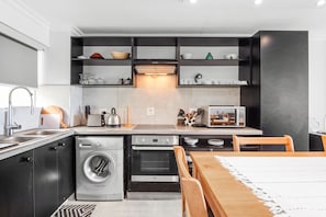 A modern kitchen with built-in appliances, a dining area with a table and chairs, and a washing machine. - Cozumel 308 (eMdloti)