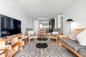 A modern living room with a large flat-screen TV, wooden furniture, a sofa, and a dining area in the background. - Cozumel 308 (eMdloti)