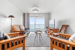 A modern living room with wooden furniture, a patterned rug, and a large window with a view of the sea. - Cozumel 308 (eMdloti)
