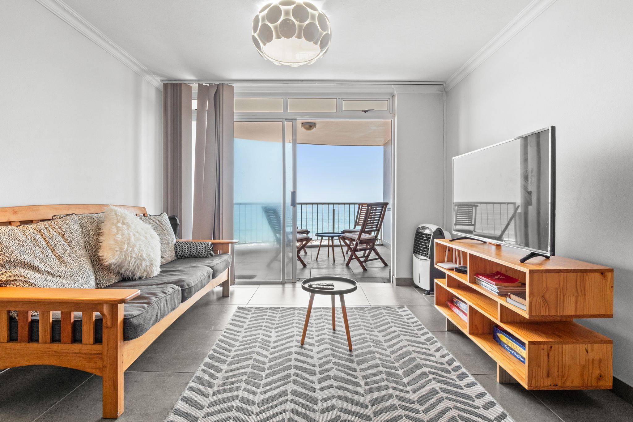 A modern living room with a sofa, a coffee table, a TV stand, and a balcony with a view.