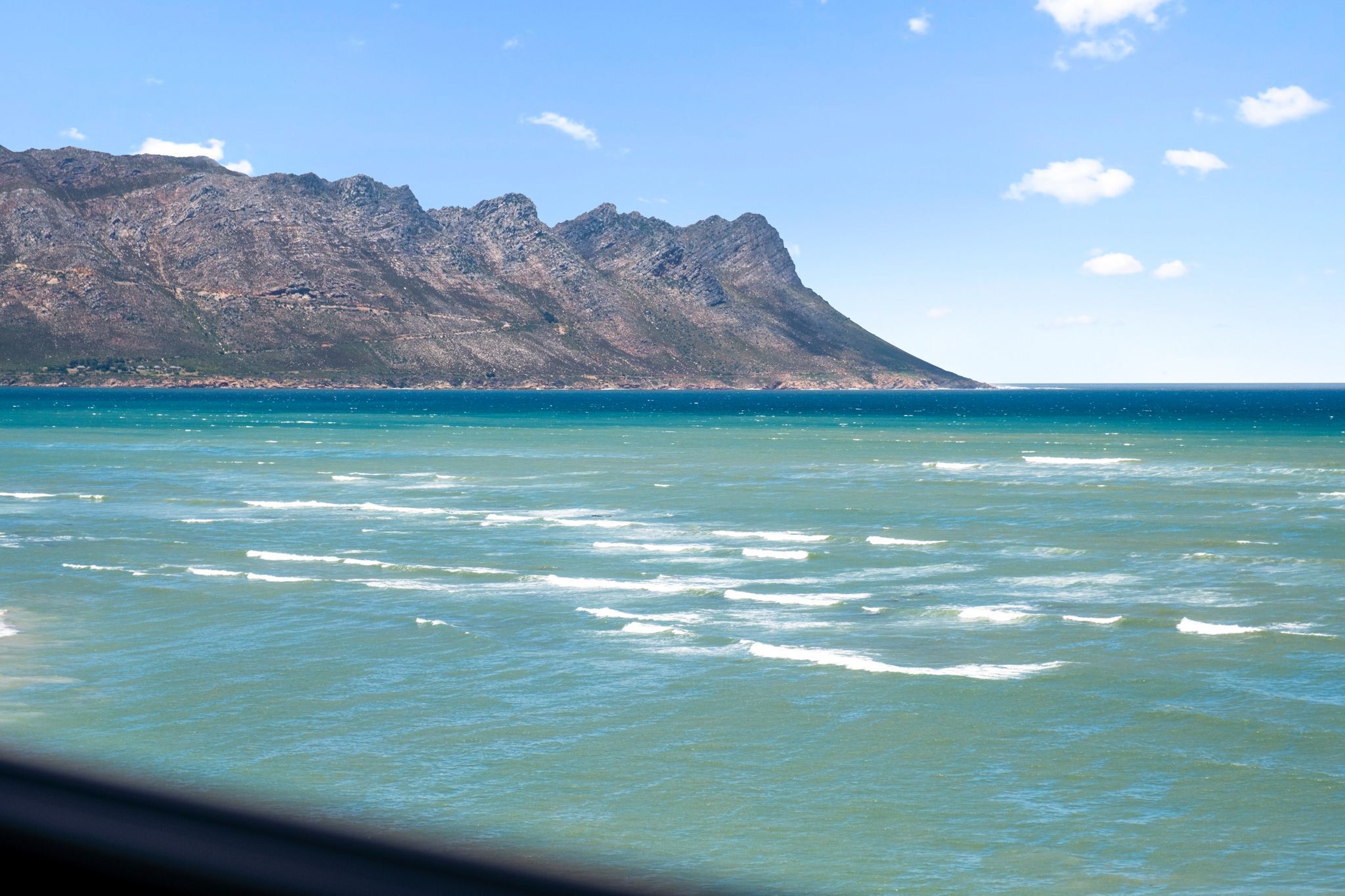 A coastal view with clear blue water and a mountain in the background.