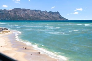 Una spiaggia con acque cristalline, una montagna rocciosa sullo sfondo e alcune persone che camminano lungo la riva.