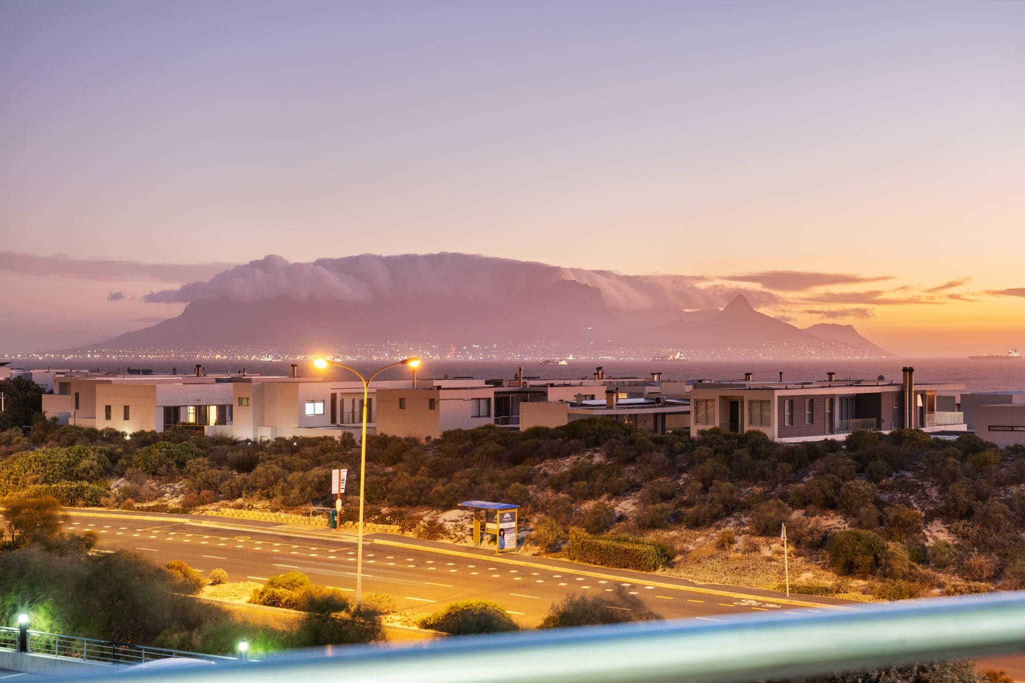 A modern building complex with multiple structures, a road with streetlights, and a mountain in the background.
