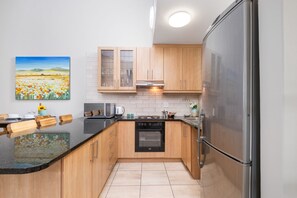 A modern kitchen with wooden cabinets, a stainless steel refrigerator, and a painting of a field on the wall. - Seaside Village B22 (Cape Town)