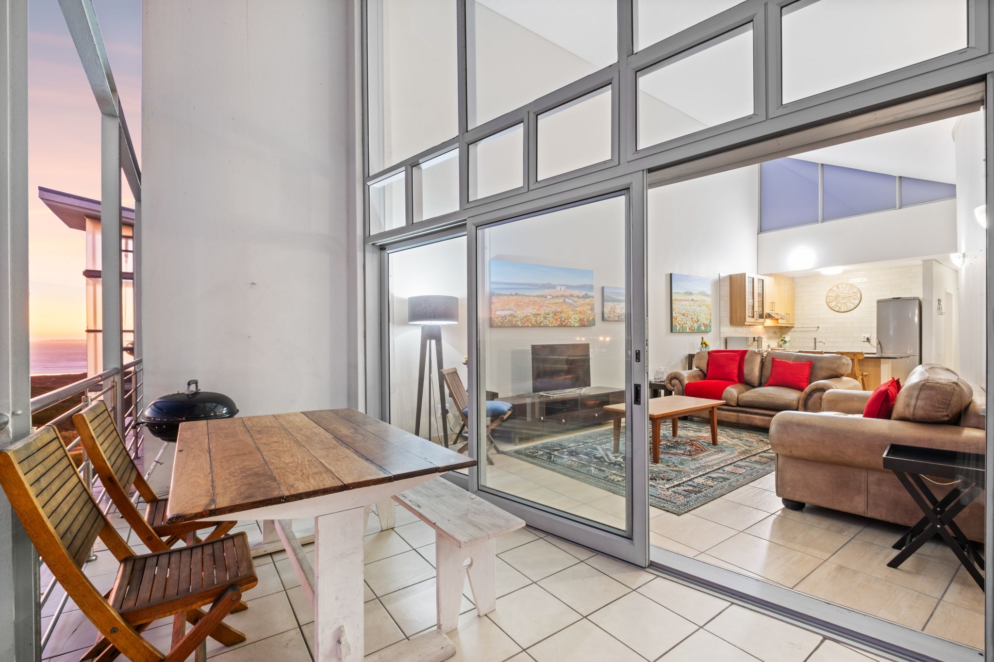 A spacious living area with a large sliding glass door leading to a balcony, a cozy seating area with a sofa and armchairs, and a wooden table with chairs.
