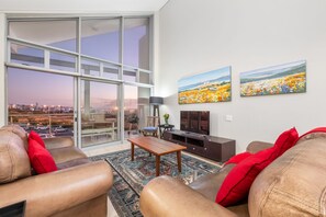 A modern living room with leather sofas, a wooden coffee table, and a large glass door leading to a balcony with a city view. - Seaside Village B22 (Cape Town)