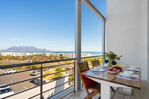 A balcony with a table set for dining, overlooking a parking area and a mountainous landscape. - Seaside Village B22 (Cape Town)