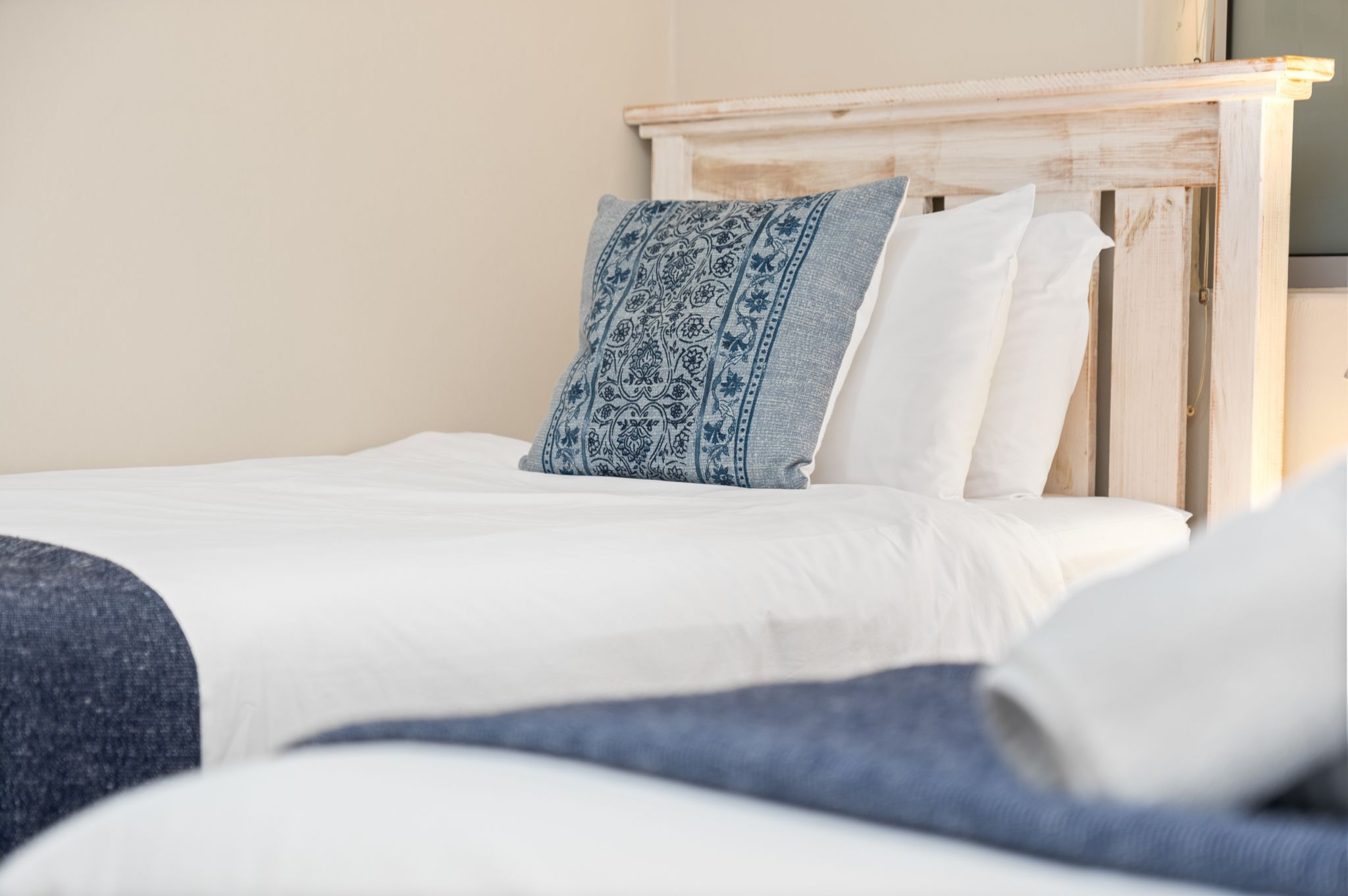 A neatly made bed with a wooden headboard, white bedding, and a blue patterned pillow.