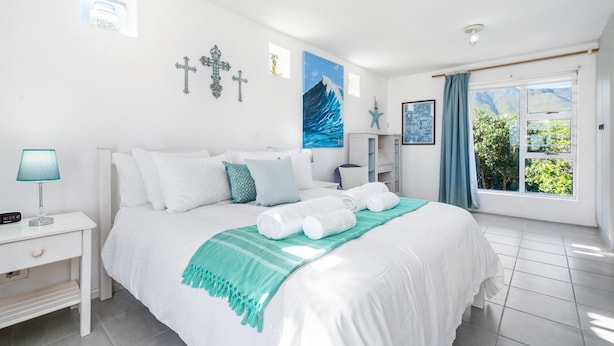 Une chambre d’hôtel avec un grand lit, du linge de lit blanc, un plaid de couleur turquoise et une vue sur la verdure par la fenêtre.