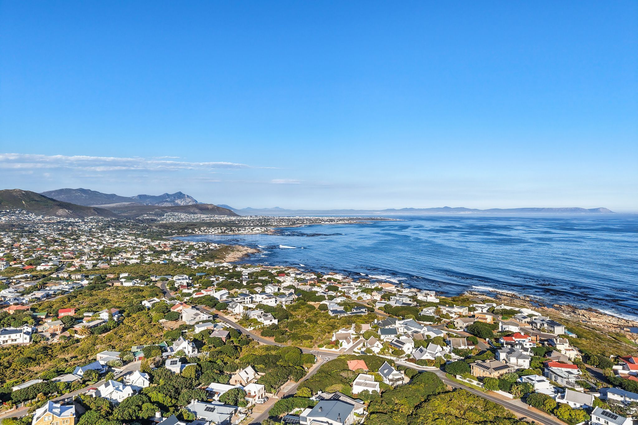 Ein Küstenwohngebiet mit Häusern, Straßen und Blick auf den Ozean und die Berge.