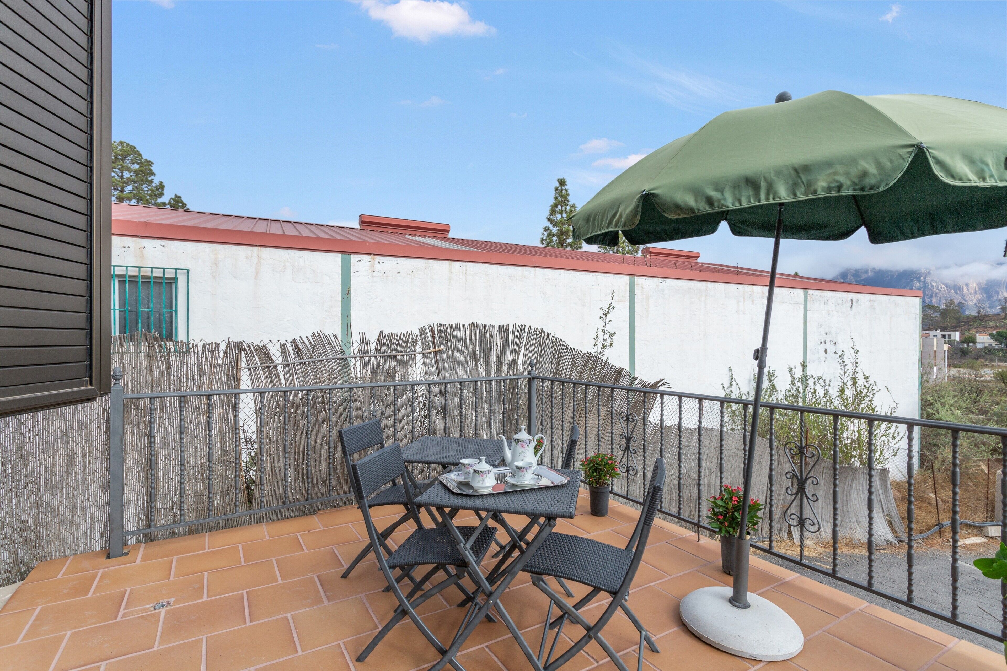Un balcon avec une table dressée pour deux personnes, un parasol vert et une plante en pot.