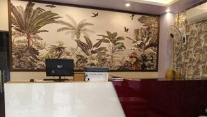 Una reception con una scrivania, un piccolo tavolo e un murale raffigurante piante tropicali.