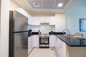 A modern kitchen with stainless steel appliances, white cabinetry, and a black countertop. - 108-Bloomfileds Cozy STU in Park View  (Abu Dhabi)