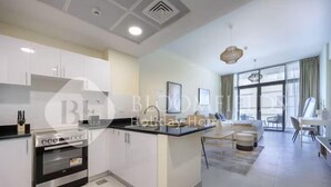 A modern kitchen with white cabinetry, a built-in oven, and a dining area with a table and chairs. - 108-Bloomfileds Cozy STU in Park View  (Abu Dhabi)