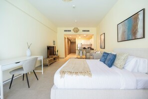 A hotel room with a bed, a desk, a chair, a TV, and a kitchenette in the background. - 108-Bloomfileds Cozy STU in Park View  (Abu Dhabi)
