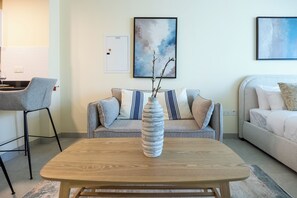 A modern living room with a wooden coffee table, a sofa with striped pillows, and a decorative vase with branches. - 108-Bloomfileds Cozy STU in Park View  (Abu Dhabi)