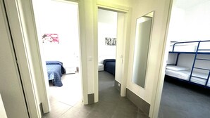 Un pasillo con una cama litera a la derecha, una puerta que da a un dormitorio y un suelo de baldosas.