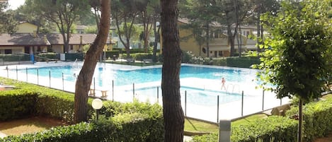 A swimming pool surrounded by trees and a well-maintained hedge.