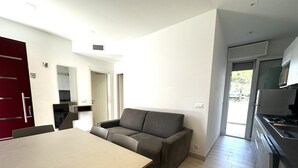 Ein moderner Wohnraum mit Essbereich, einem grauen Sofa, einer Küche mit Herd und einer roten Tür.