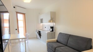 A modern kitchen with a dining area, a grey sofa, and a TV. - Very comfortable seafront apartment (Bibione)
