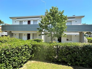 Um edifício moderno de dois andares com telhado plano, entrada coberta e uma pequena árvore no centro.