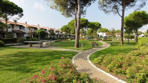 Un sentier traversant un parc, avec des bancs, des arbres et une aire de jeux en arrière-plan.