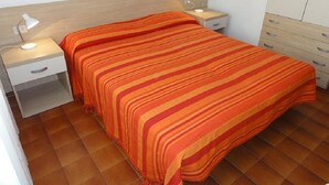 Un dormitorio con una cama, dos mesitas de noche con lámparas, un armario y suelo de baldosas.